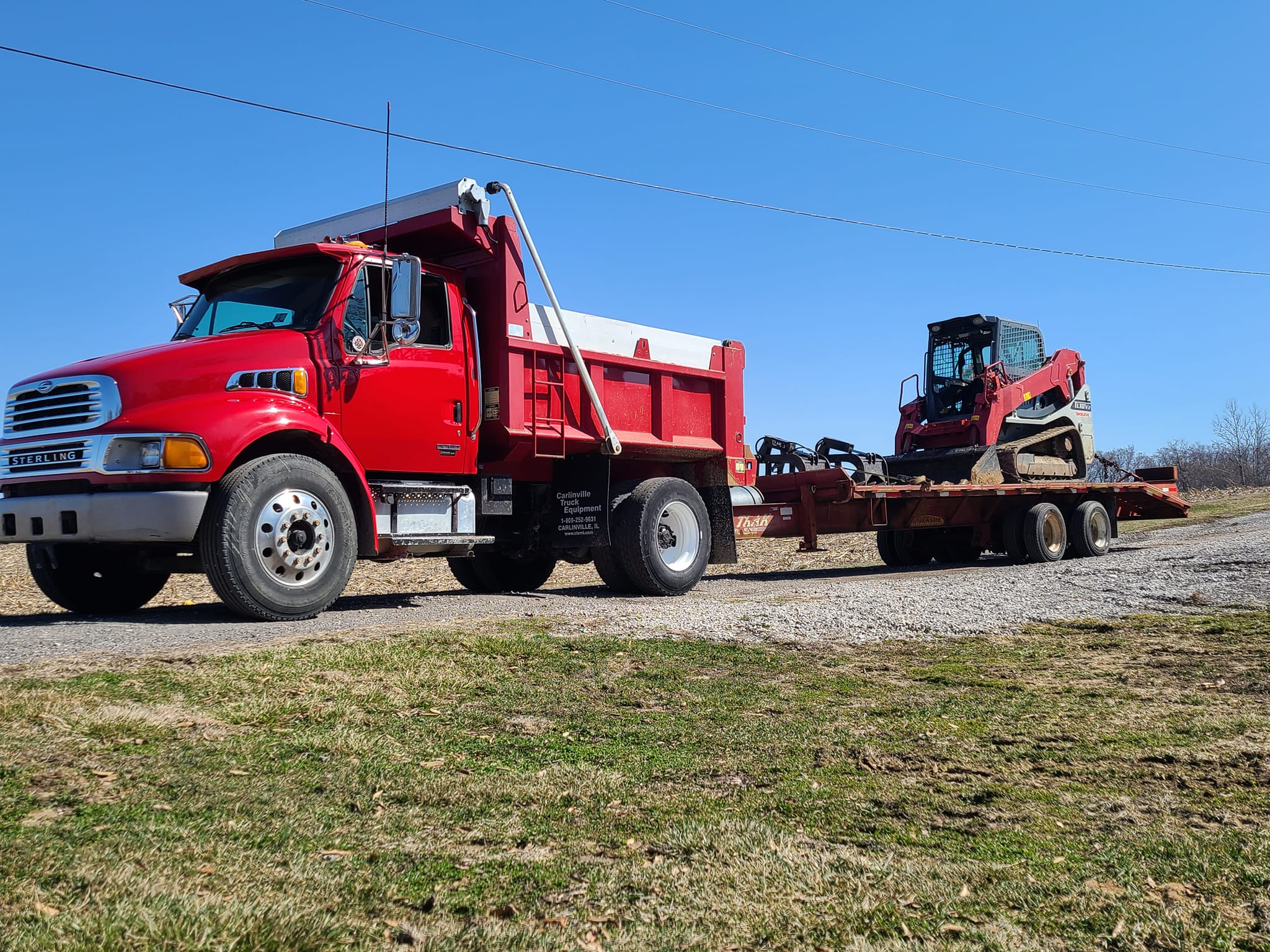Dump truck hauling skid steer on trailer